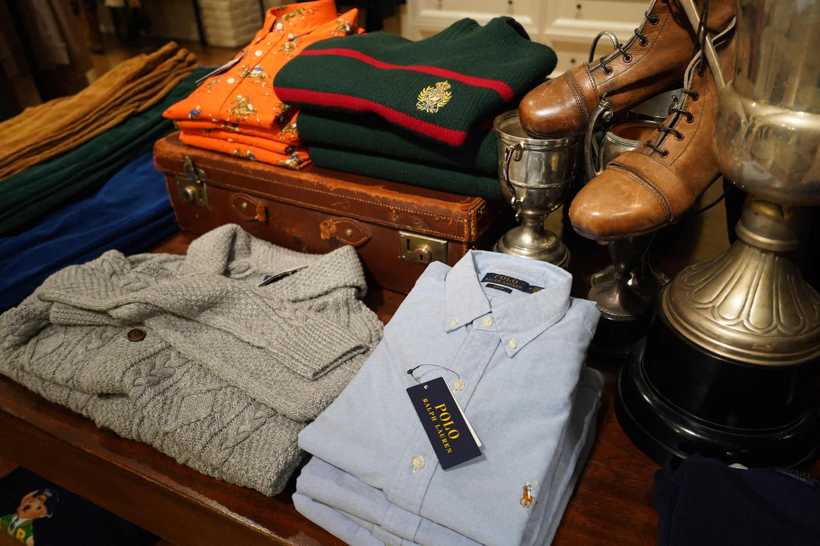 Folded Polo Ralph Lauren sweaters, shirts, and vintage props styled on a wooden table — showcasing classic American heritage design.